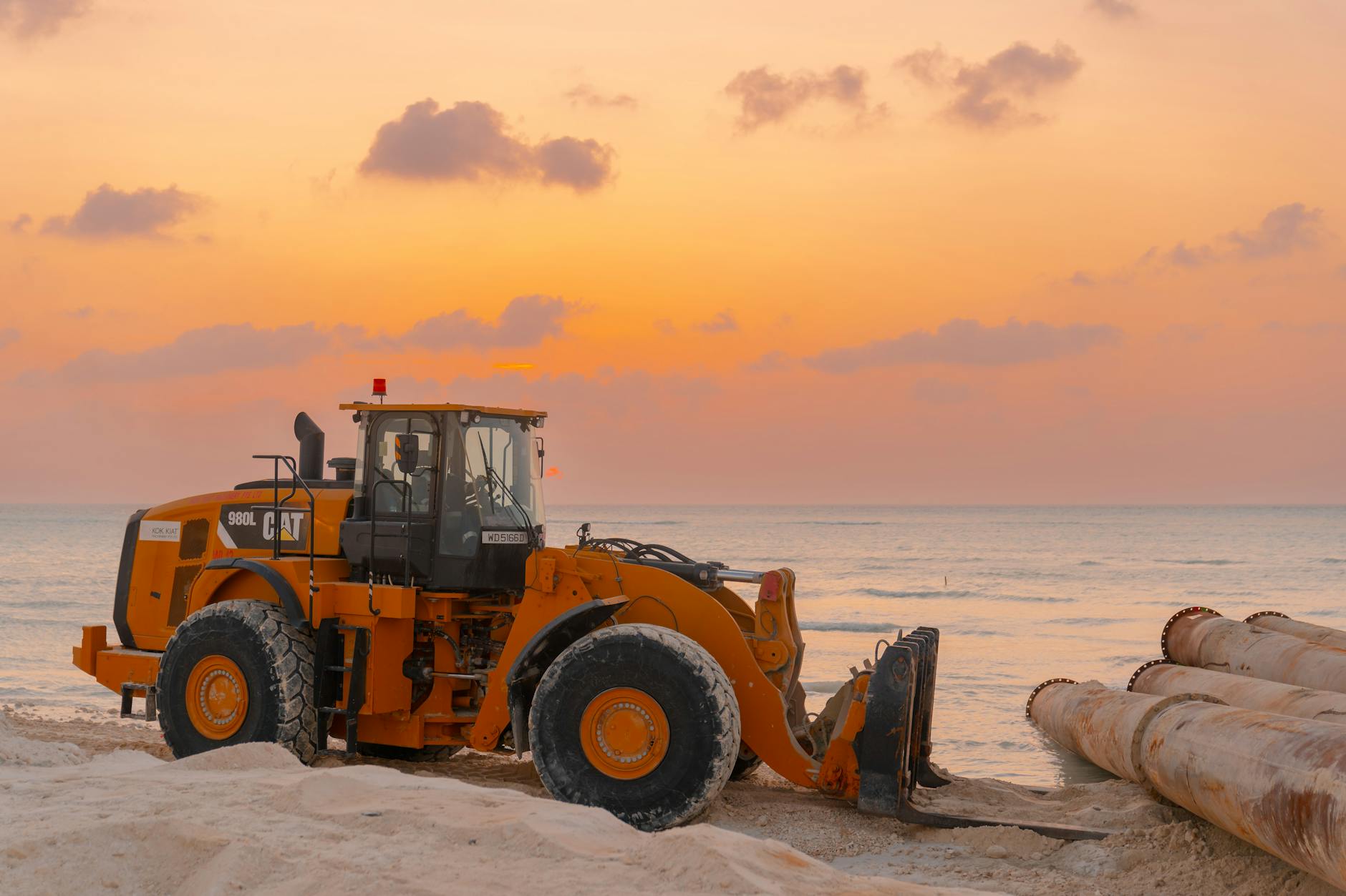 a bulldozer moving large pipes on a beach construction site with a stunning sunset backdrop bulldozer moving large pipes on a beach construction site during sunset